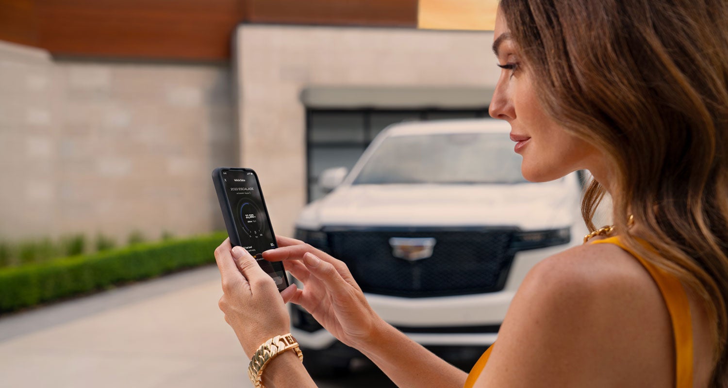 lady checking her mobile with a Cadillac vehicle background | Clay Cooley Cadillac in Mesquite TX